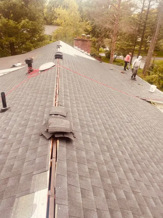Workers repairing a large gray shingled roof.